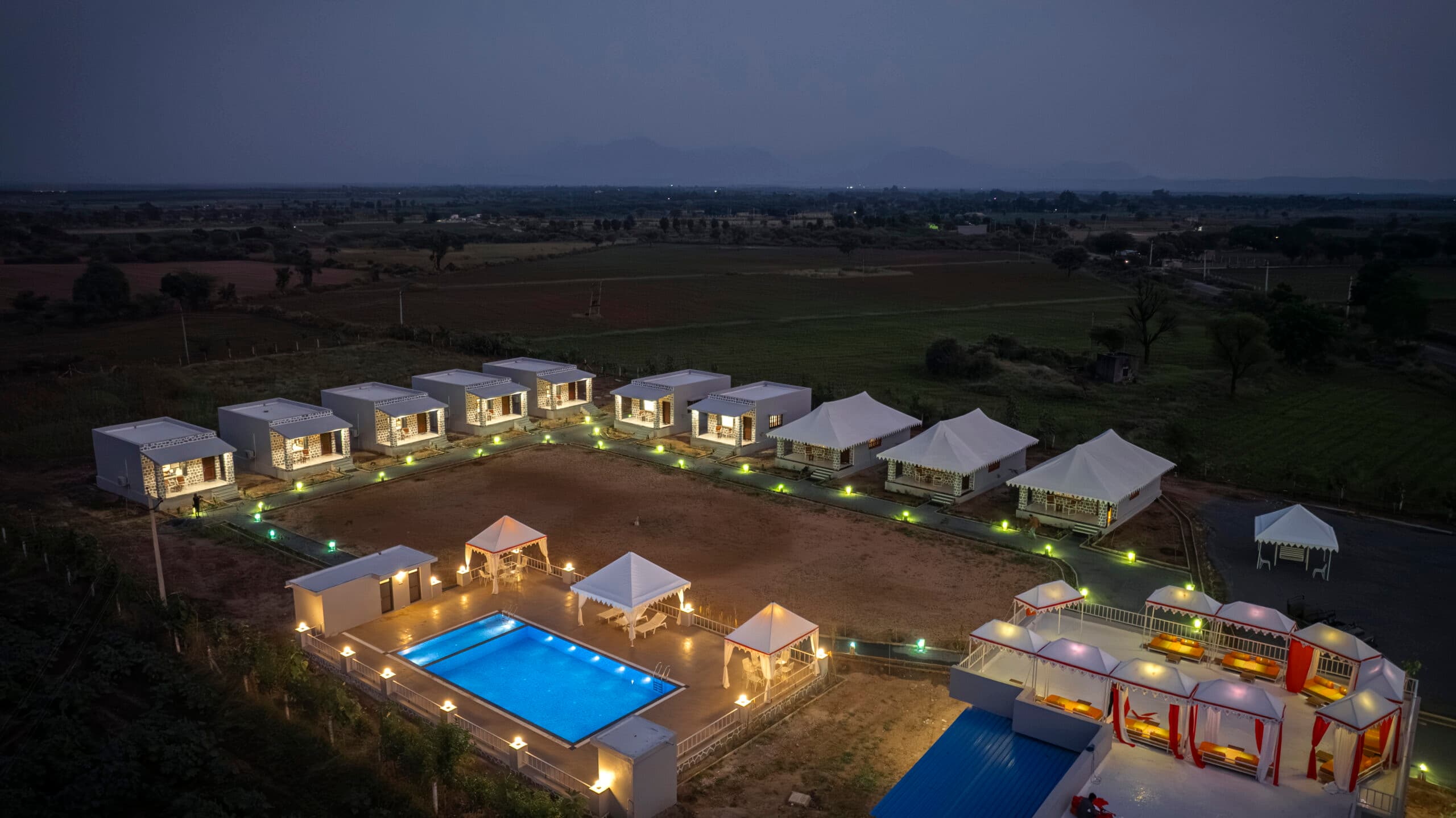 Upvan Jawai from the air at dusk, the pool lit blue among the cottages