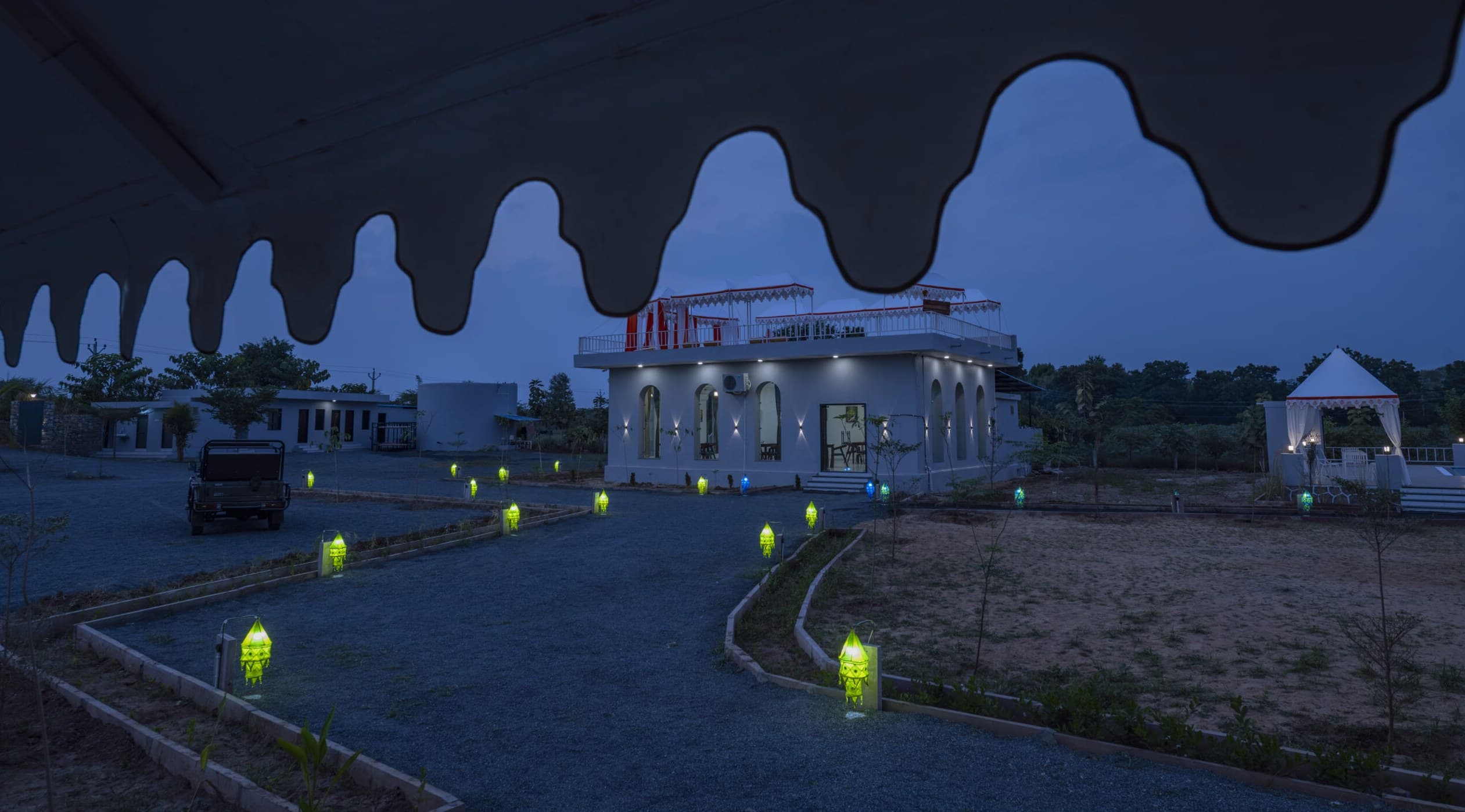 The scalloped canopy over the drive at Upvan Jawai at blue hour, garden lamps lit