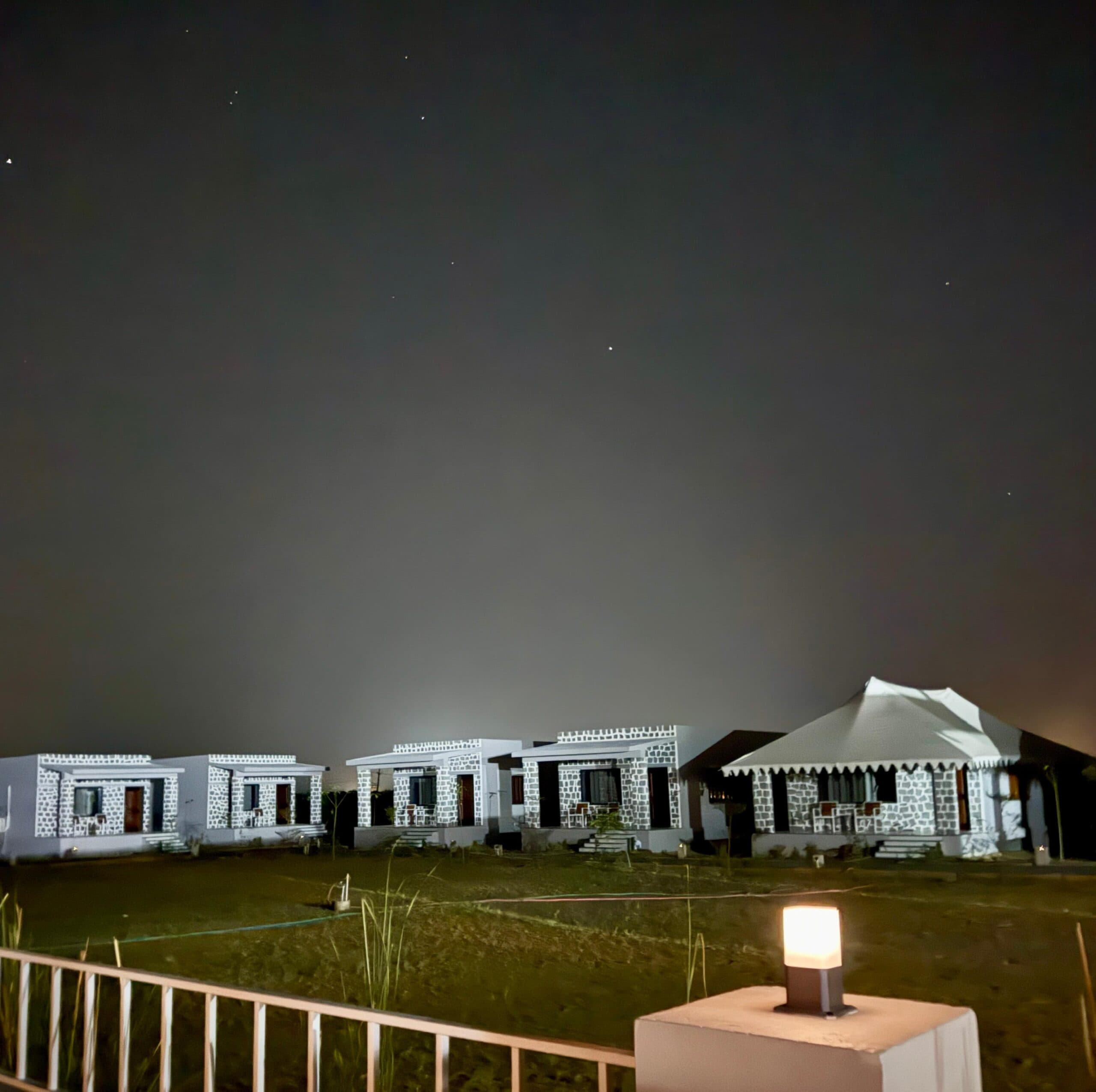 A lantern glowing on the lawn at Upvan Jawai with the lit cottages behind