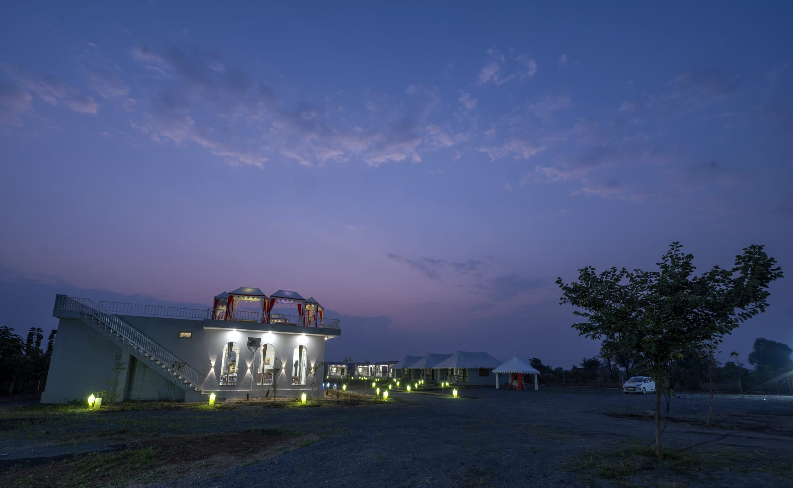 The main building at Upvan Jawai lit up at dusk, the cottages along the lawn